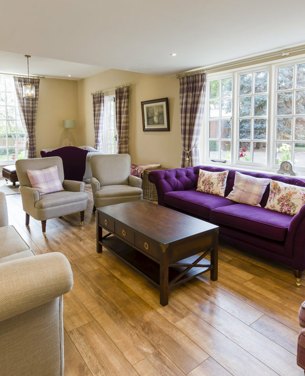 clean and quaint living room set up with purple sofa and checked curtains