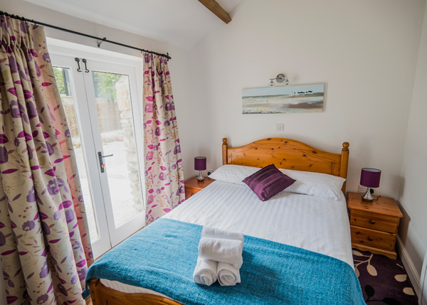 simple bedroom set up, wooden furniture and purple furnishings with wide patio style windows