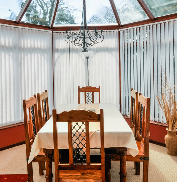 sunlit dining room with wooden table and chairs featuring a chandelier and vertical blinds inviting space for meals